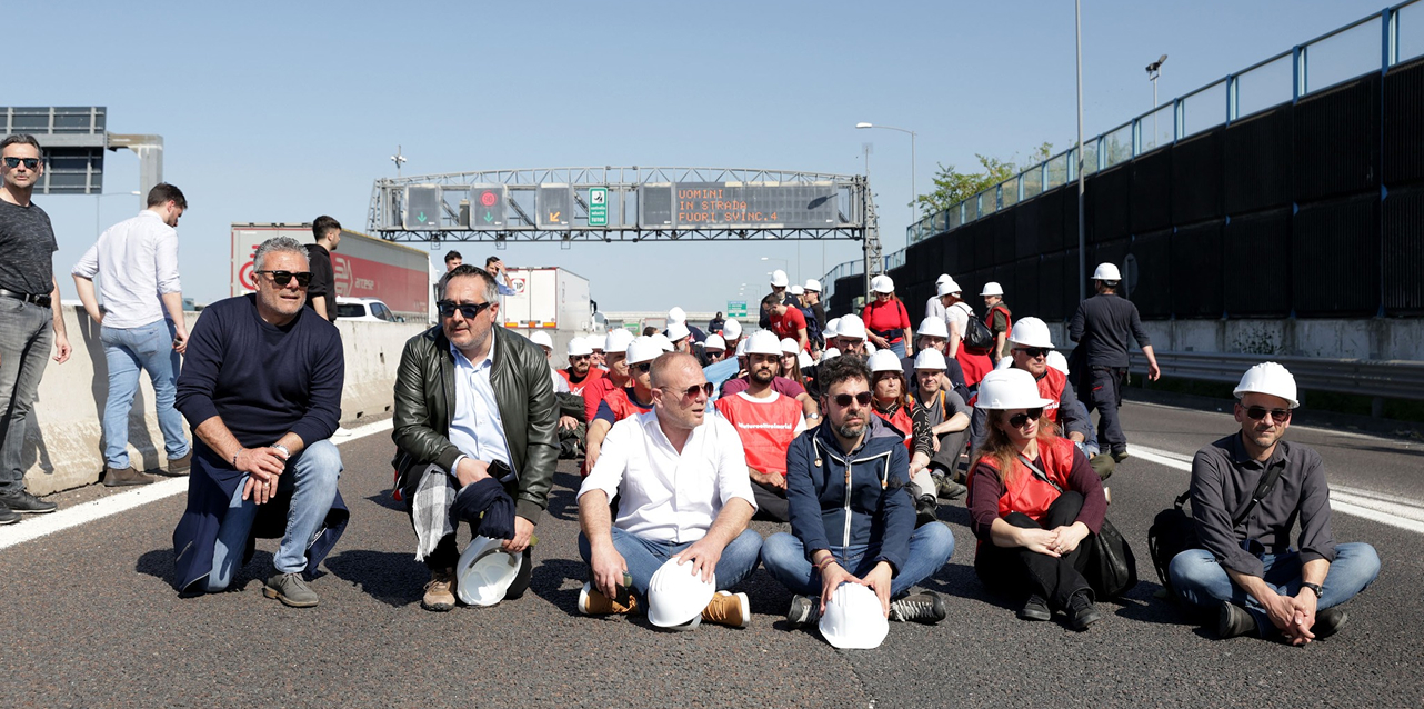 Copertina della rivista 'News dal Sindacato' della FenealUIL su un tavolo in legno, accanto a un casco da cantiere giallo, strumenti da lavoro e rotoli di progetti. Testo: 'Leggi il nuovo numero della rivista della FenealUIL'.