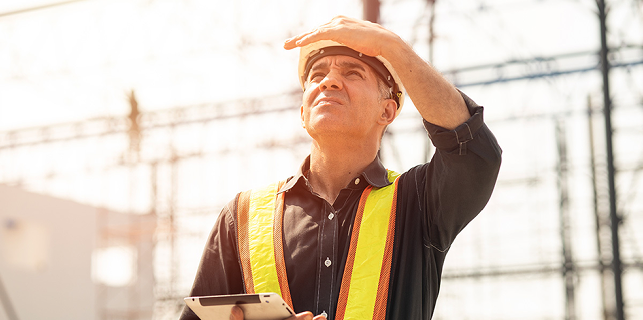 Copertina della rivista 'News dal Sindacato' della FenealUIL su un tavolo in legno, accanto a un casco da cantiere giallo, strumenti da lavoro e rotoli di progetti. Testo: 'Leggi il nuovo numero della rivista della FenealUIL'.
